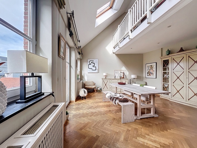 A warm penthouse living room with herringbone parquet and a mezzanine, in central Brussels